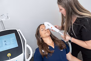 A woman is getting a facial treatment in a clinic by another woman who is wearing a black shirt and a watch.