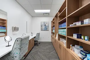 An empty room with white walls, a desk with a mirror, and a shelf filled with various products in blue and white boxes.