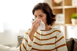 A woman is blowing her nose while sitting on a couch.