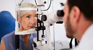 Optometrist examining an older woman's eye with a slit lamp