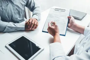 Two people sitting at a table with documents and a tablet