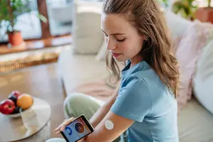 A girl is sitting on the couch and using a cell phone with a bracelet on her arm.