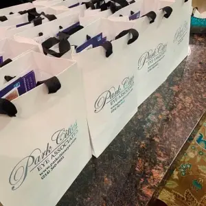 Several white paper bags with blue and black handles and logos are arranged on a marble surface.