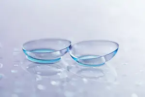 Two clear glass contact lenses sitting on a white surface with water droplets around them