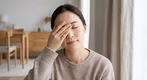A woman sitting in a chair in a room, rubbing her eyes