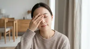 A woman sitting in a chair in a room, rubbing her eyes