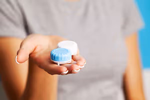 A person holding a pair of blue and white colored contact lenses in their hand.