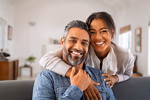 A man and woman are sitting on a couch in a living room, smiling and posing for a photo.