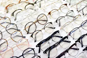 Many eyeglasses with different frames and lenses are neatly arranged on a white surface, possibly for sale in an optical store.