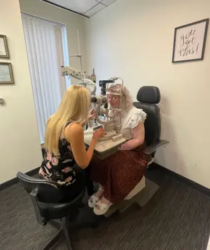 An adult woman is getting an eye exam from a female doctor inside of an eye clinic
