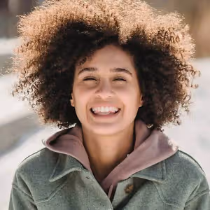 Woman with a curly afro hairstyle smiling in a winter setting