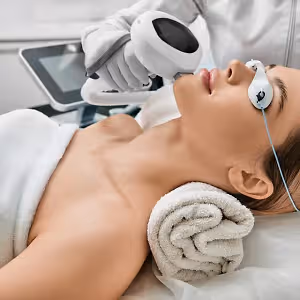 A woman is undergoing a laser treatment at a beauty salon with a white towel on her body and neck