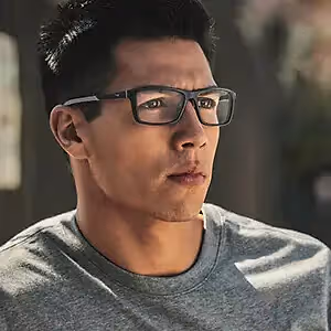 Man wearing glasses and a gray shirt posing for a photo with a blurry background.