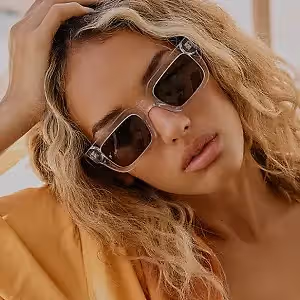 Woman with blonde wavy hair wearing sunglasses and a peach top looking down
