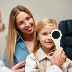 A young girl smiles as a doctor checks her eye with a tool in a clinic