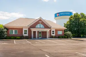 A building named Dayton Optic Center is situated in front of a water tower with a blue and white sign reading 'Montgomery County'. There are several trees, bushes, and plants in the area.