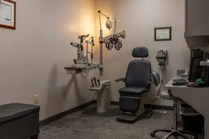 A medical room with an eye examination equipment and a chair with a footrest and a monitor on a desk.