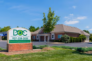 Dayton Optometric Center sign in front of a brick building with a tree and green lawn