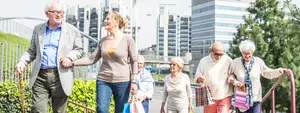 A group of elderly people are walking down the street, one of them holding a cane and smiling