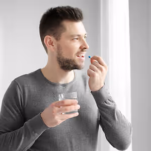 man holding glass of water and glaucoma medication