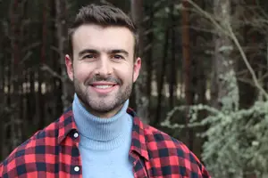 A man with a beard is smiling and posing for a photo in a forest area