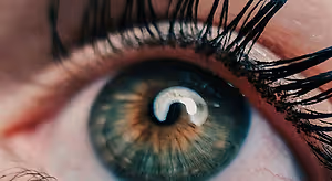 Close-up of a woman's eye with long eyelashes, slightly blurry iris, and a reflection of light