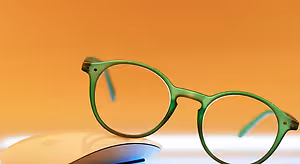 A pair of green-framed glasses sitting on top of a white mouse against an orange background