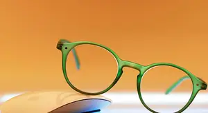 A pair of green-framed glasses sitting on top of a white mouse against an orange background
