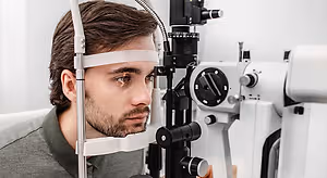 A man wearing glasses sits in front of an eye exam machine and looks into it