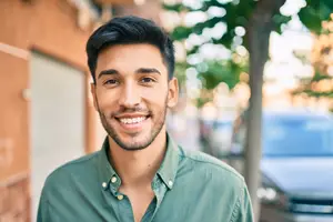 Smiling man with a beard and mustache wearing a green polo shirt standing outside on a sunny day