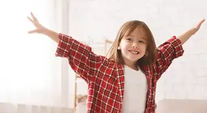 A girl with her arms out, smiling, wearing a red and white checkered long-sleeve shirt