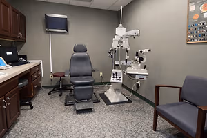 A room with a medical examination chair, an ophthalmoscope, and a computer monitor, all set up for eye examinations