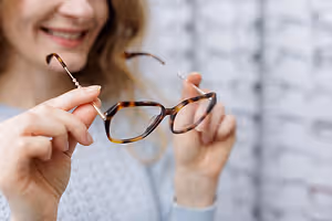 A woman with a smiley face is holding a pair of glasses