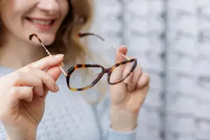 A woman with a smiley face is holding a pair of glasses