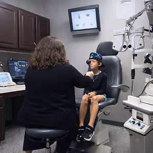 A woman examining a child's eyes in a medical office with an optometrist machine in the background.