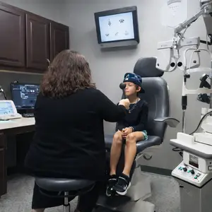 A woman examining a child's eyes in a medical office with an optometrist machine in the background.