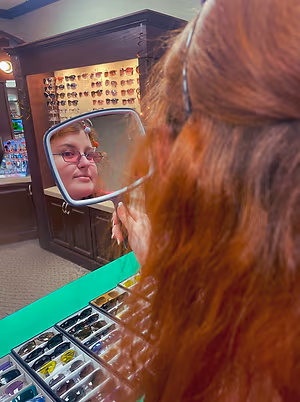 A woman wearing glasses is looking at herself in a mirror in a shop.