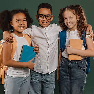 Three children smiling and posing for a photo with backpacks and books