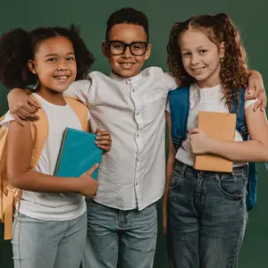 Three children smiling and posing for a photo with backpacks and books