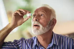 An old man using eye drops in his eye