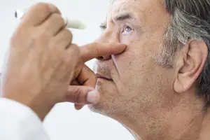 An elderly man is receiving an eye exam by a doctor who is administering eye drops.