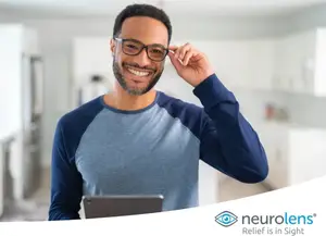 A smiling man with glasses is adjusting his glasses while looking at something on a tablet.