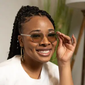 An adult woman with curly hair is wearing a white shirt and gold hoop earrings, and she is adjusting her glasses and smiling. She seems to be posing for a photo.