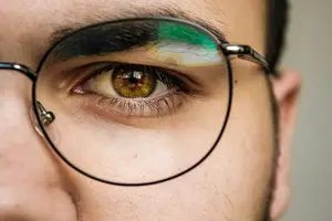 A close-up of a man's eye with green and yellow paint on the top of the glasses