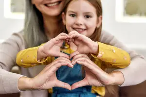 A woman and a little girl forming a heart shape with their hands