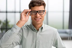 A man adjusting his glasses while smiling and looking at the camera