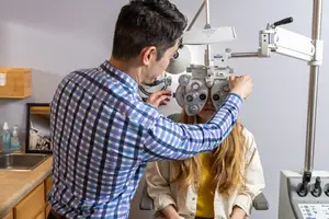 A man is adjusting an eye exam machine on a woman in a clinic