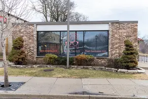 A brick building with a glass window and a reflection of a car, along with plants and a tree in front.