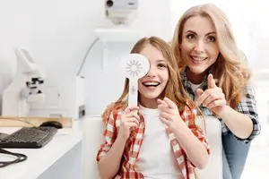 A woman and a girl are smiling and looking at a sunburst object in a dental clinic.