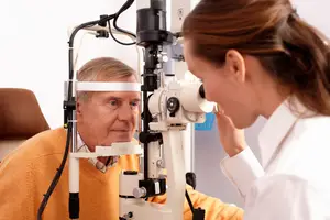 An elderly man is undergoing an eye examination by a female doctor in a clinic